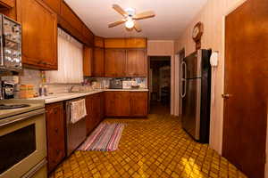Kitchen with light countertops, appliances with stainless steel finishes, brown cabinets, and a ceiling fan