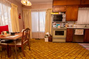 Kitchen with brown cabinetry, stainless steel dishwasher, light countertops, electric stove, and light colored carpet