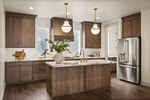 Kitchen featuring high end fridge, dark wood-style floors, decorative light fixtures, a kitchen island with sink, and dark brown cabinetry