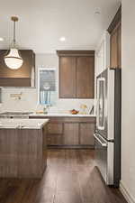 Kitchen featuring high end refrigerator, dark wood-type flooring, custom range hood, tasteful backsplash, and pendant lighting