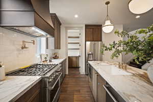 Kitchen with light stone counters, appliances with stainless steel finishes, custom range hood, hanging light fixtures, and recessed lighting