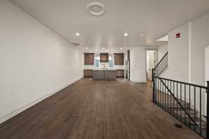 Unfurnished living room featuring recessed lighting, dark wood-style flooring, a textured ceiling, and stairway