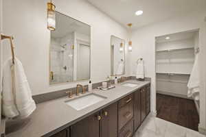 Bathroom with double vanity, a shower stall, a spacious closet, light marble finish flooring, and recessed lighting