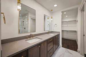 Bathroom with double vanity, a shower stall, a walk in closet, light marble finish flooring, and recessed lighting