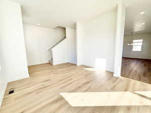 Unfurnished living room featuring light wood-style flooring, stairs, recessed lighting, and a chandelier
