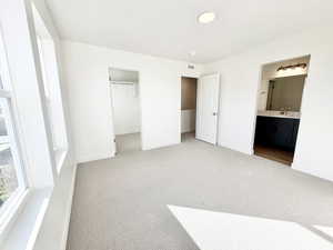 Unfurnished bedroom with a spacious closet, light colored carpet, and connected bathroom