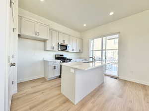 Kitchen featuring light wood-style floors, stainless steel appliances, recessed lighting, a kitchen island with sink, and light stone counters