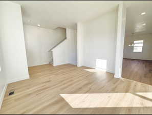 Unfurnished living room with light wood-style floors, stairs, recessed lighting, and a chandelier