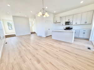 Kitchen with open floor plan, pendant lighting, a center island with sink, a chandelier, and white cabinetry