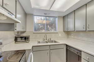 Kitchen featuring gray cabinets, appliances with stainless steel finishes, under cabinet range hood, and light countertops