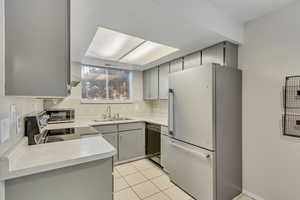 Kitchen with appliances with stainless steel finishes, gray cabinets, light countertops, light tile patterned floors, and extractor fan