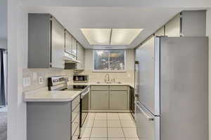 Kitchen with stainless steel appliances, gray cabinets, light countertops, light tile patterned flooring, and under cabinet range hood