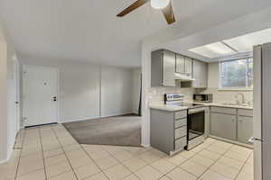 Kitchen featuring gray cabinetry, stainless steel appliances, light countertops, light colored carpet, and a ceiling fan