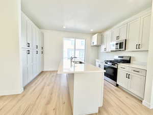 Kitchen with appliances with stainless steel finishes, white cabinets, an island with sink, light stone counters, and light wood finished floors