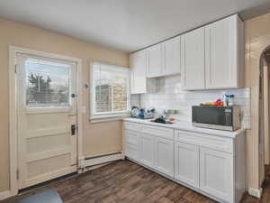 #31 (Upstairs 1-bedroom): Kitchen featuring white cabinetry, a baseboard heating unit, LVP flooring, and white backsplash