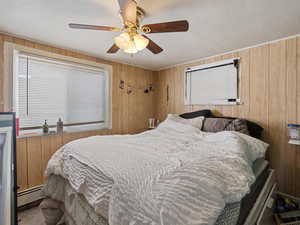 #39 (Basement 1-bedroom): Bedroom with ceiling fan, a baseboard radiator, and wood paneling walls