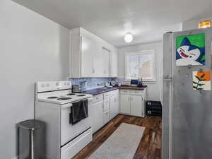 #37 (Upstairs 2-bedroom): Kitchen featuring white electric range, freestanding refrigerator, dark wood-style flooring, white cabinetry, and decorative backsplash