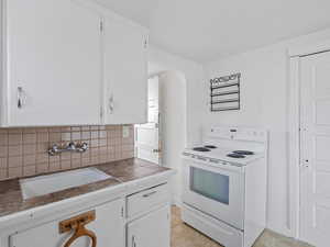 #29 (Basement Studio): Kitchen with white cabinetry, white electric range, backsplash, and arched walkways