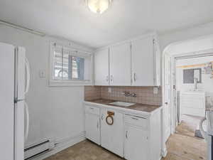#29 (Basement Studio): Kitchen with white cabinetry, a baseboard heating unit, refrigerator