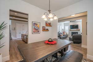 Dining space with dark wood-type flooring, a glass covered fireplace, a chandelier, a ceiling fan, and beamed ceiling