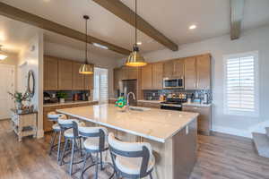 Kitchen featuring tasteful backsplash, decorative light fixtures, appliances with stainless steel finishes, brown cabinets, and beam ceiling