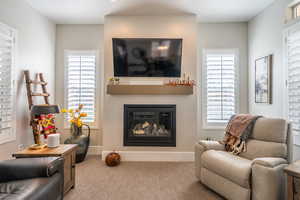 Carpeted living area featuring a glass covered fireplace and baseboards