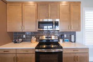 Kitchen with stainless steel appliances, light stone countertops, decorative backsplash, and brown cabinets