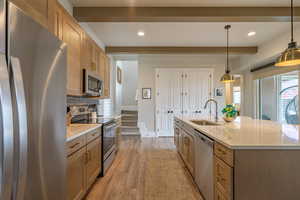 Kitchen featuring stainless steel appliances, pendant lighting, light stone countertops, recessed lighting, and light wood-style flooring