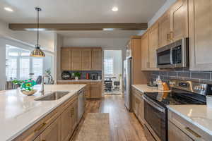 Kitchen with stainless steel appliances, pendant lighting, backsplash, light stone countertops, and light wood-style floors