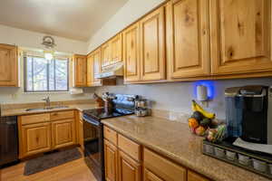 Kitchen featuring black range with electric stovetop, light stone counters, under cabinet range hood, and light wood-style flooring