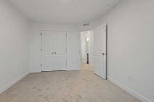 Unfurnished bedroom with light carpet and a closet