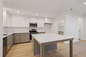 Kitchen featuring gray cabinetry, appliances with stainless steel finishes, recessed lighting, light wood finished floors, and light stone counters