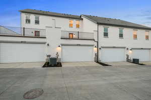 Rear view of house featuring concrete driveway, stucco siding, a balcony, and an attached garage
