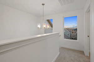Hall featuring light carpet and a chandelier