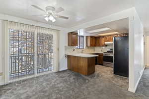 Kitchen featuring light countertops, freestanding refrigerator, a peninsula, brown cabinets, and stainless steel gas stove