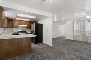 Kitchen featuring light countertops, appliances with stainless steel finishes, dark carpet, ceiling fan, and decorative backsplash