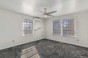 Spare room with a textured ceiling, dark carpet, a ceiling fan, and a wall mounted AC