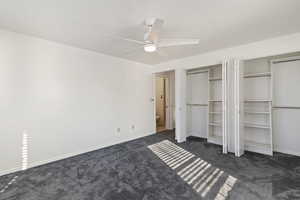 Unfurnished bedroom featuring dark carpet, multiple closets, and ceiling fan