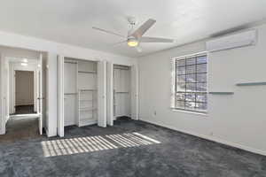 Unfurnished bedroom featuring multiple closets, dark carpet, a wall mounted AC, and ceiling fan