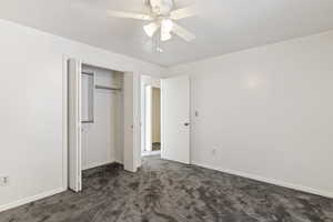 Unfurnished bedroom featuring dark carpet, a closet, and a ceiling fan