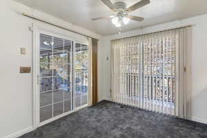 Unfurnished room with dark colored carpet, ceiling fan, and a textured ceiling