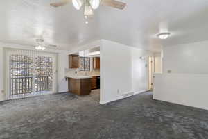 Unfurnished living room featuring dark colored carpet, a textured ceiling, and a ceiling fan