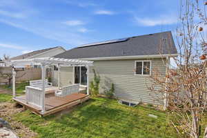 Back of property featuring a shingled roof, a wooden deck, a yard, a pergola, and roof mounted solar panels