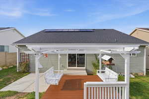 Back of property featuring roof with shingles, roof mounted solar panels, a wooden deck, and a pergola