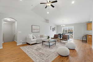 Living room featuring light wood-type flooring, vaulted ceiling, ceiling fan, arched walkways, and recessed lighting