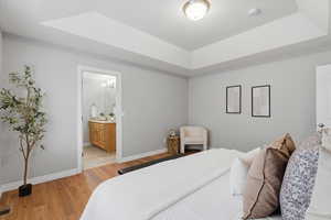Bedroom featuring a raised ceiling, light wood-style floors, and ensuite bath