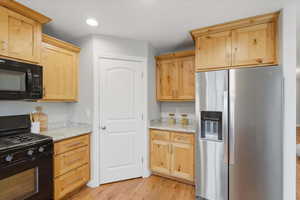 Kitchen with light brown cabinets, black appliances, light stone counters, and light wood-style floors