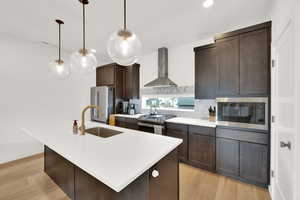 Kitchen featuring dark  cabinetry, stainless steel appliances, an island with sink, and pendant  light fixtures