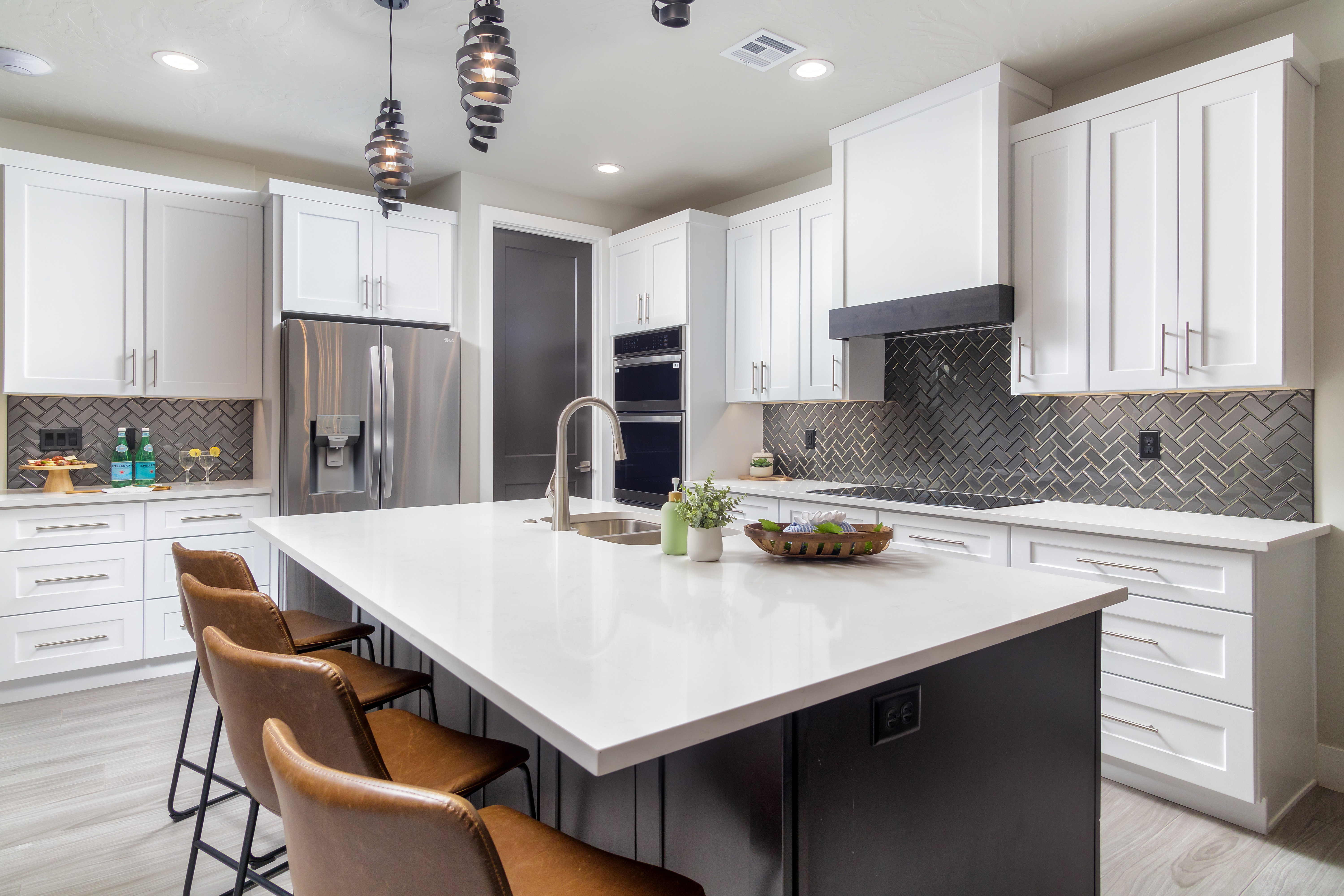 Kitchen featuring a kitchen island with sink, a breakfast bar area, white cabinetry, hanging light fixtures, and light stone countertops