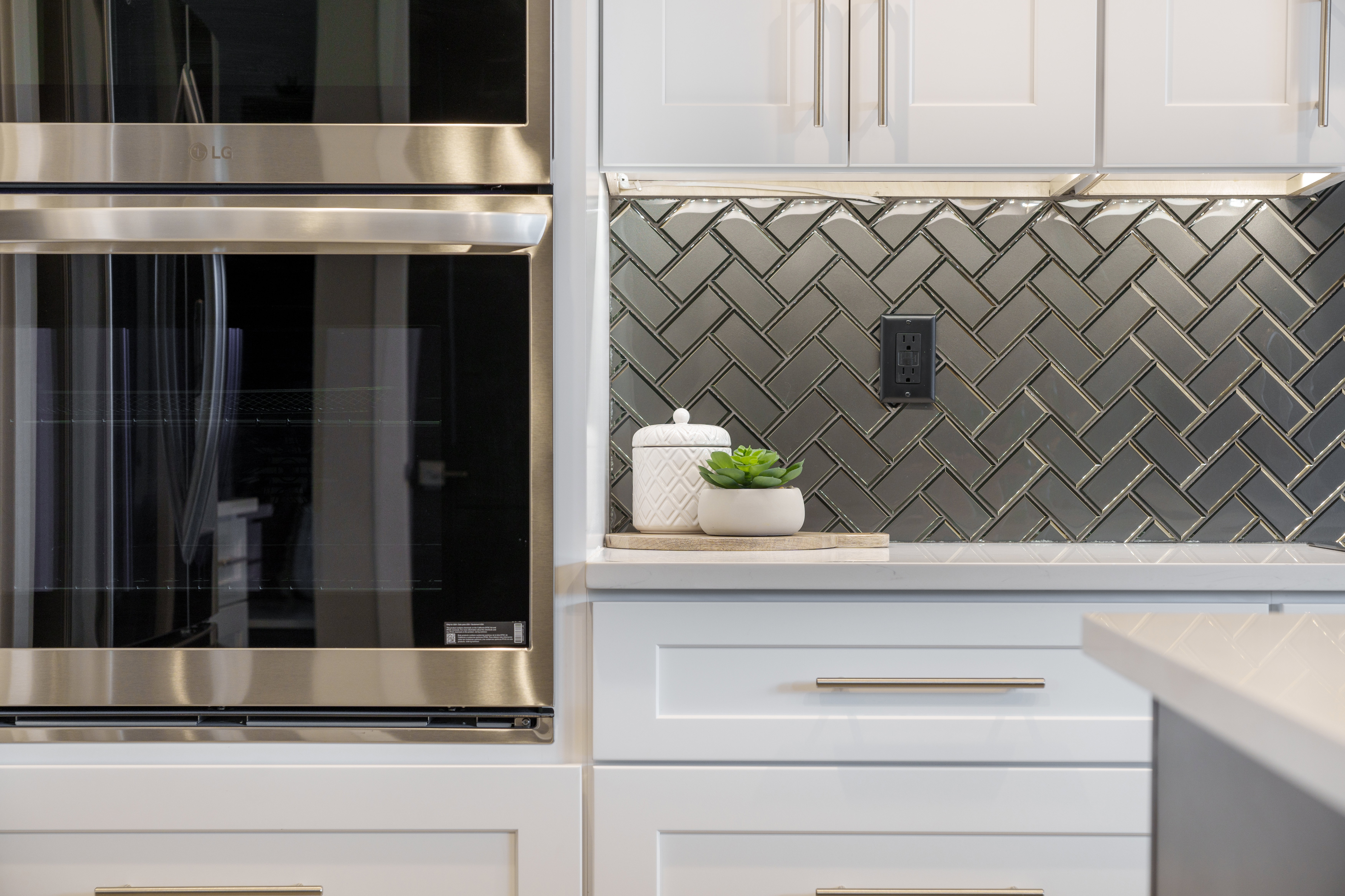 Kitchen with white cabinetry, stainless steel double oven, decorative backsplash, and light stone countertops